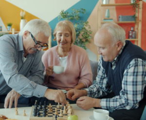 Three elderly friends playing chess together while enjoying coffee in a living room