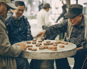Group of elderly men playing a traditional board game together at an outdoor stone table